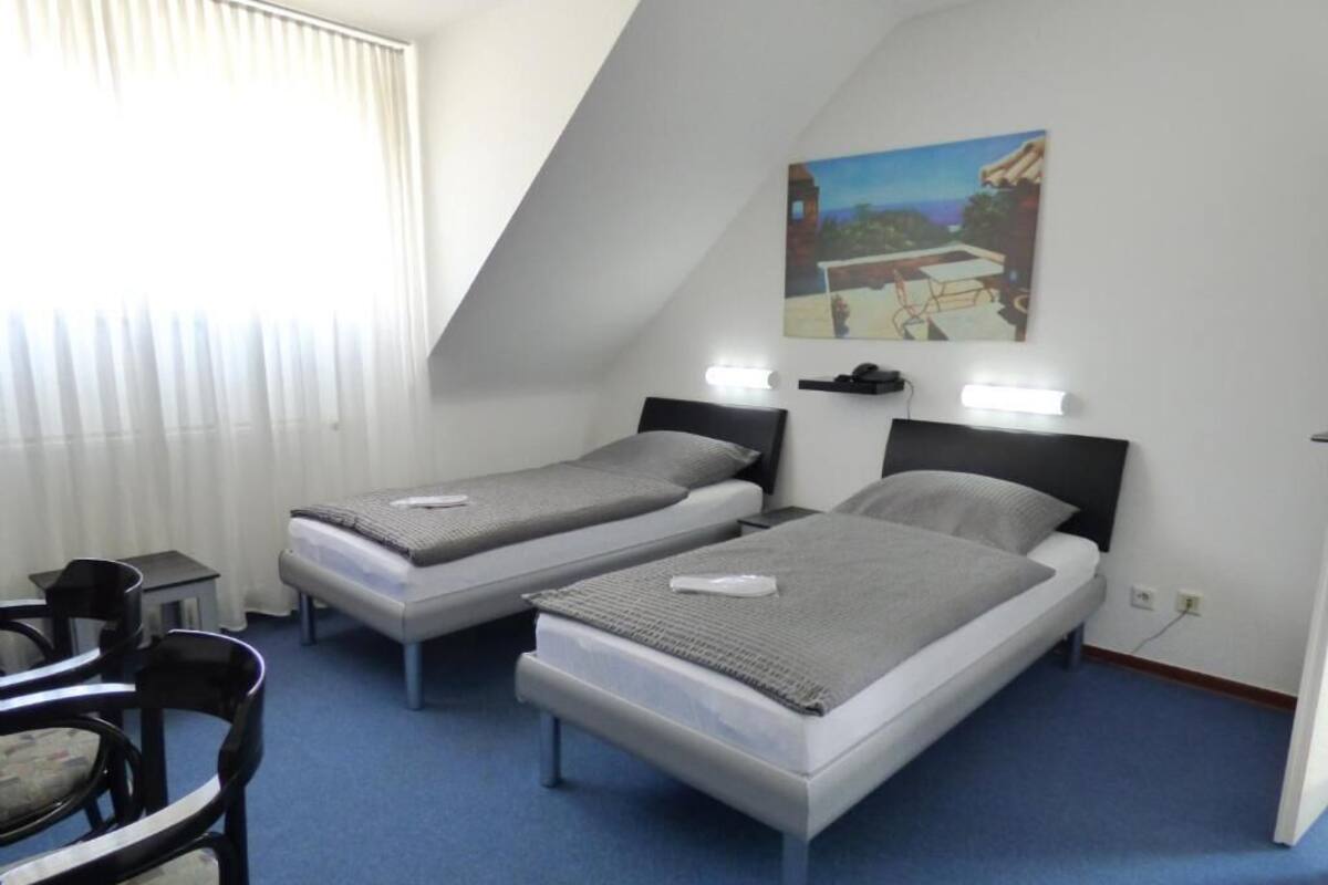A room with two beds, a desk, a chair, and a painting on the wall.