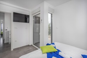 A modern bedroom with a bed, a TV mounted on the wall, and a sliding glass door leading to an outdoor area. - Dramalj luxury villa - pool, whirlpool & sea view (Dramalj)