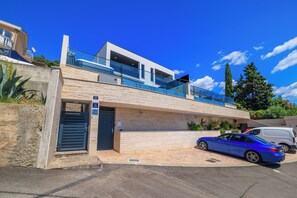 A modern two-story building with a balcony, a garage, and a parked car. - Dramalj luxury villa - pool, whirlpool & sea view (Dramalj)