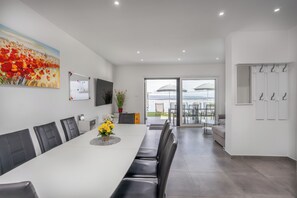 A modern dining area with a long table, black chairs, a painting, and a view through glass doors to an outdoor seating area. - Dramalj luxury villa - pool, whirlpool & sea view (Dramalj)