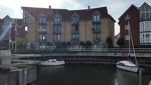 A waterfront building with multiple windows and balconies, a bridge with flags, and two boats docked at a marina. - Vacation apartment Marina Liebe directly in the City Marina Cuxhaven (Cuxhaven)
