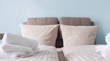 A bed with checkered bedding and two pillows, a folded white towel, and a light blue wall.