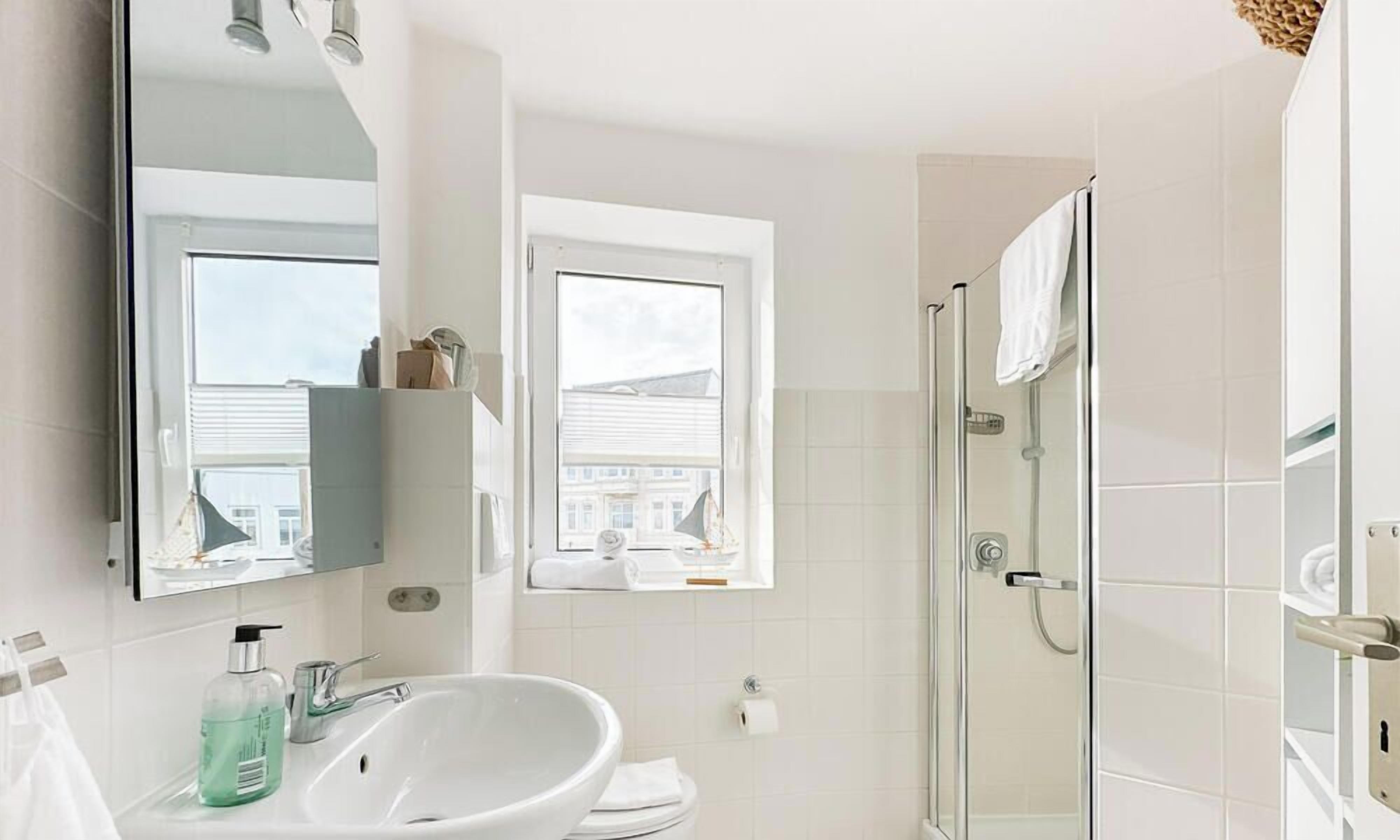 Een moderne badkamer met een grote spiegel, een wastafel, een douchecabine van glas en een raam met uitzicht op gebouwen.