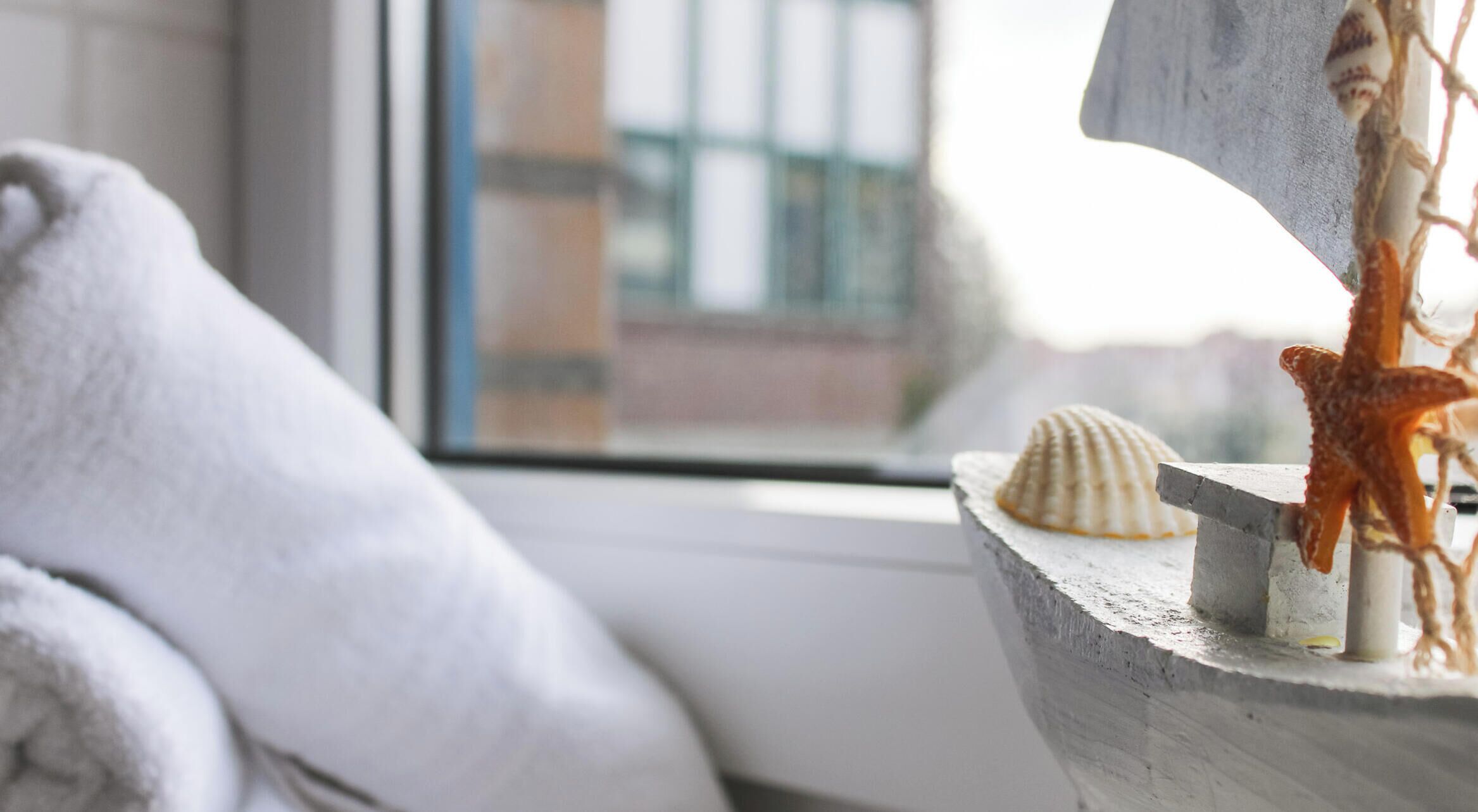 Una finestra con vista sugli edifici, un asciugamano bianco e una struttura in legno con conchiglie e una stella marina.