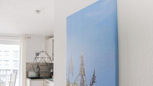 A modern kitchen with a geometric pendant light, a large window, and a painting of a cityscape on the wall. - Vacation apartment Marina Liebe directly in the City Marina Cuxhaven (Cuxhaven)