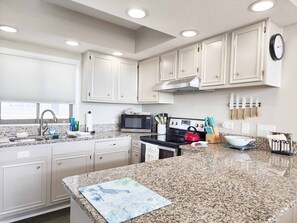 A kitchen with white cabinets, a microwave, stove, and granite countertops. - Litchfield Retreat 613 - North Litchfield, Balcony, Ocean View (Pawleys Island)