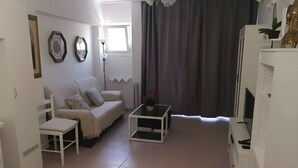 A living room with a white sofa, a small table with a vase, a white cabinet, and a large window with curtains. - A charming refuge in San Telmo (Puerto de la Cruz)