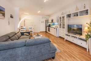 A modern living room with a grey sofa, a dining table, and a kitchen area with white cabinets and a built-in oven. - Cozy vacation apartment Edda - close to the beach in the heart of Zinnowitz (Zinnowitz)