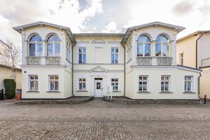A symmetrical building with a central entrance, flanked by two wings with balconies. - Cozy vacation apartment Edda - close to the beach in the heart of Zinnowitz (Zinnowitz)