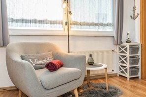 A cozy room with a grey armchair, a small round table, a radiator, and a shelf with baskets. - Cozy vacation apartment Edda - close to the beach in the heart of Zinnowitz (Zinnowitz)
