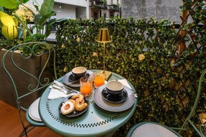 A table set with breakfast items, a lamp, and a green metal chair in an outdoor setting with a hedge backdrop. - Gian Giacomo Mora Raffinato monolocale (Milan)