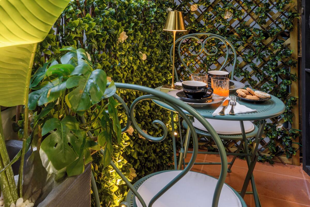 A small outdoor seating area with a metal chair and table, surrounded by lush greenery and a lattice wall.
