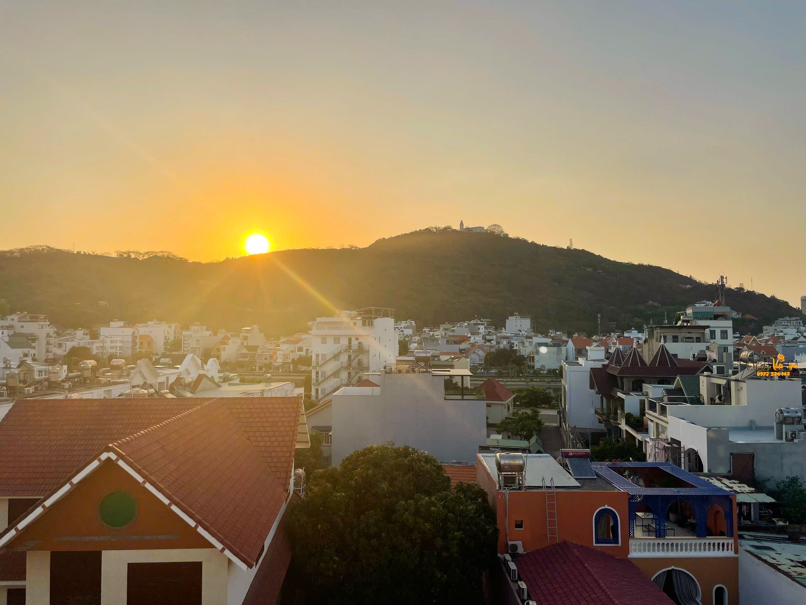 A cityscape with buildings, a river, and a hill with a tower in the background during sunset.