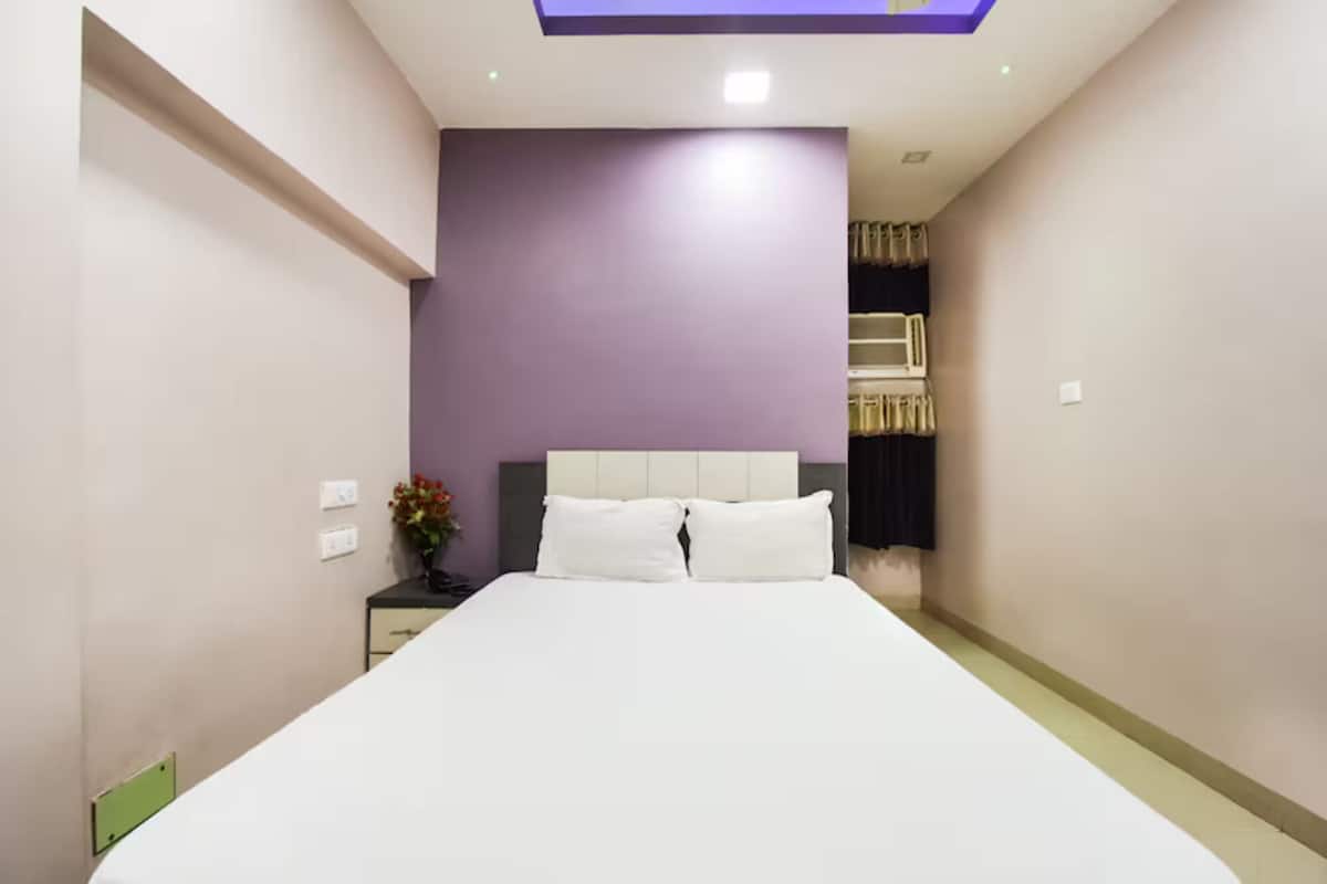 A bedroom with a bed, a nightstand, a vase with flowers, and a ceiling light.