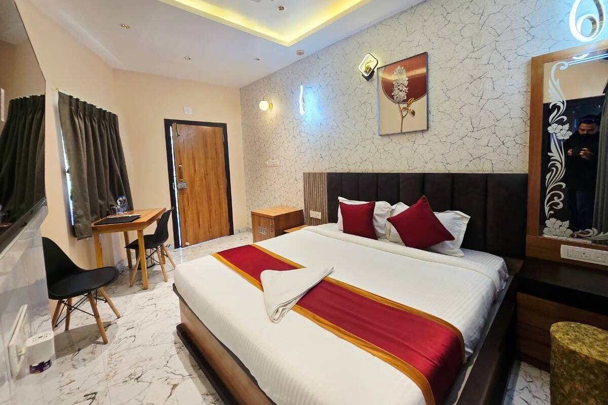 A hotel room with a large bed, a desk, a chair, a wardrobe, and a mirror.