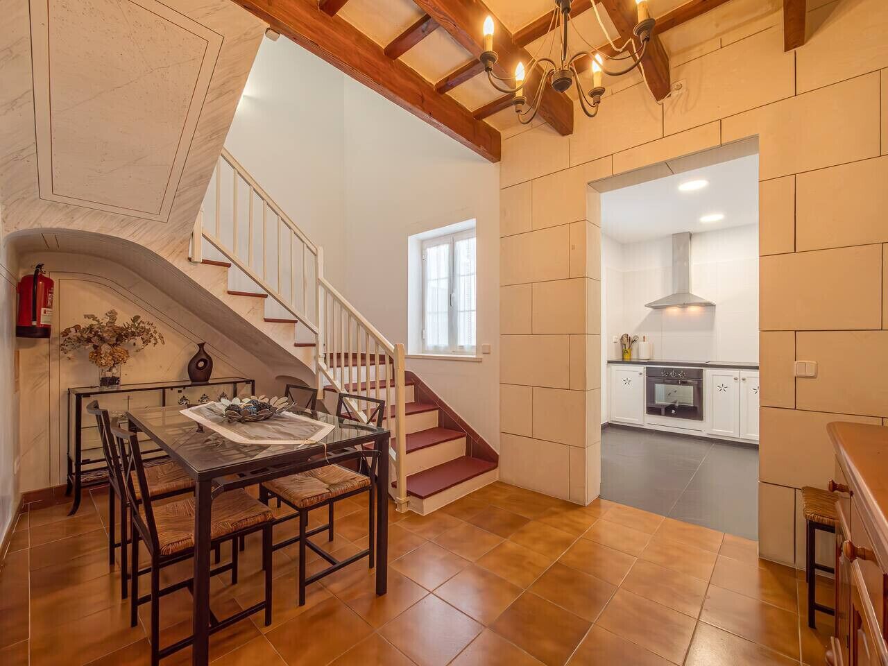 A dining area with a table and chairs, a staircase, and a kitchen in the background.