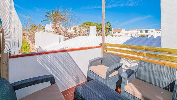 A rooftop terrace with wicker furniture, a wooden railing, and a view of buildings and trees. - Casa Major by 3 Villas Menorca (Fornells)