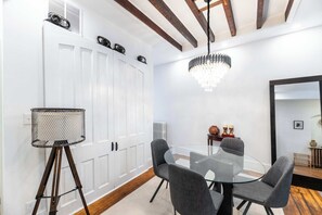 Une salle à manger moderne avec une table en verre, des chaises grises, un lustre et une porte blanche avec un radiateur.
