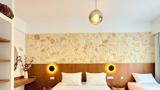 Ein Hotelzimmer mit einem großen Bett, zwei Nachttischen, einem Holzkopfstück, einer Steinwand und einer Hängeleuchte.