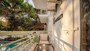 A balcony with a glass table, cushioned seating, and a pool. - Staymaster Solintra 2BHK A301 (Verem)