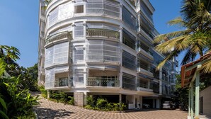 A multi-story building with balconies, a covered entrance, and a paved driveway. - Staymaster Solintra 2BHK A301 (Verem)