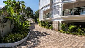 A paved pathway leading to a building with balconies, surrounded by lush greenery. - Staymaster Solintra 2BHK A301 (Verem)