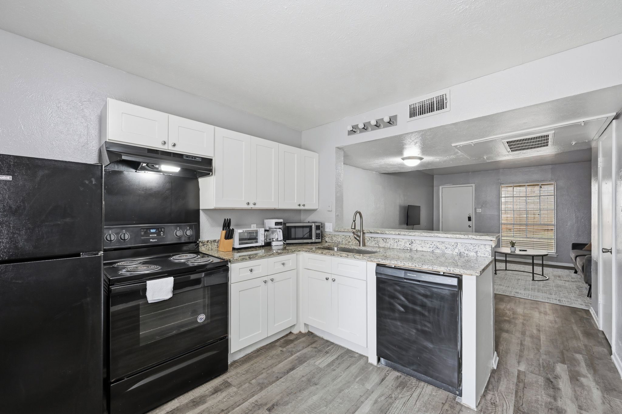 A modern kitchen with white cabinets, a black refrigerator, a stove, a microwave, and a dishwasher.