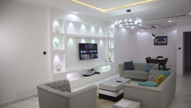 A modern living room with a flat-screen TV, a sofa, a coffee table, and a chandelier. - Jasmine Chidera Apartments (Lagos)