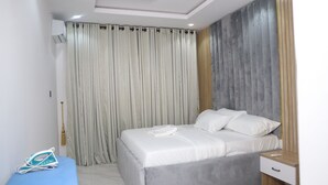 A bedroom with a bed, curtains, a bedside table, and a wall unit. - Jasmine Chidera Apartments (Lagos)