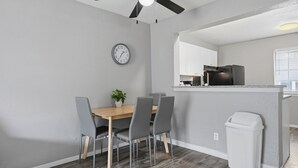 Een moderne keuken met een zwarte koelkast, een houten eettafel met vier stoelen, een plafondventilator en een klok aan de muur.