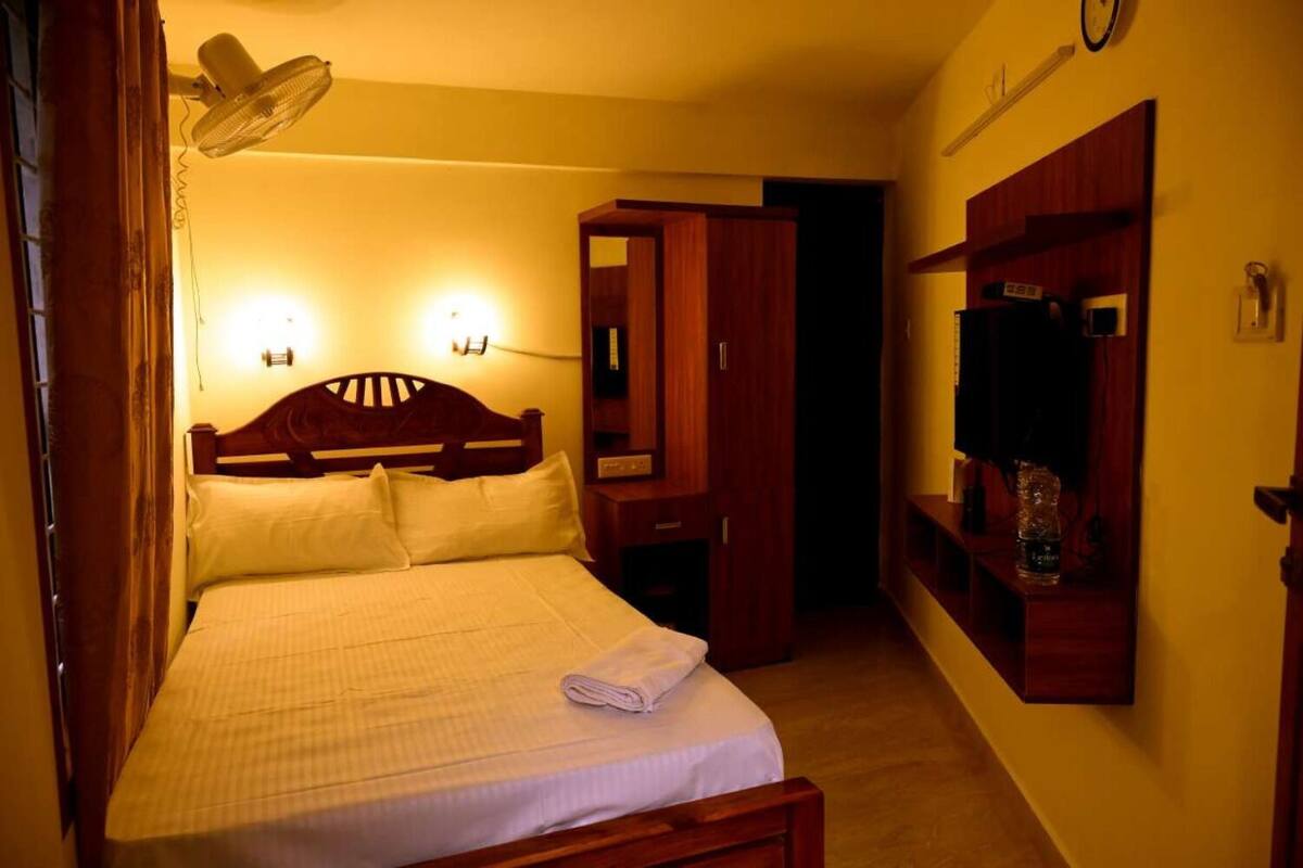 Una camera d'albergo con un letto, una lampada da comodino, una TV a muro e uno specchio.