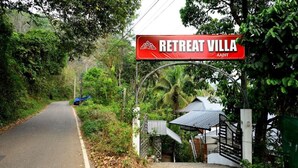 Señal de 'Retreat Villa' con entrada vigilada, rodeada de exuberante vegetación y una carretera.