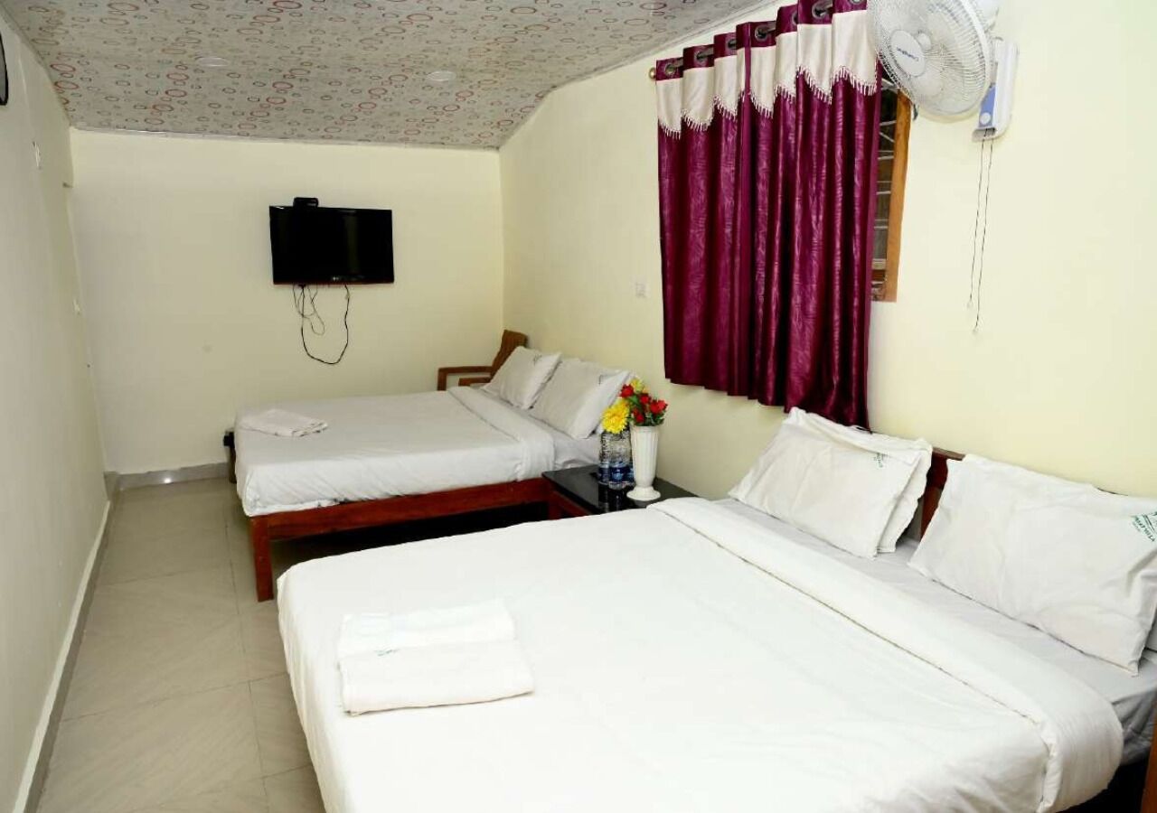 A hotel room with two beds, a flat-screen TV mounted on the wall, a ceiling fan, and a window with purple curtains.