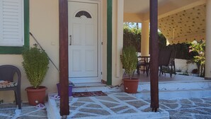 Un'area esterna coperta con pavimento in pietra, una pergola in legno, piante in vaso e una porta che dà su un ambiente interno.