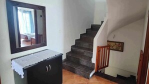 Una scala che conduce a un secondo piano, un armadio nero con un copriletto in pizzo e uno specchio appeso al muro.