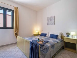 A bedroom with a bed, bedside tables, a window with curtains, a wall-mounted artwork, and a tiled floor. - Residence Il Ciliegio with swimming pool - Apartment 2 (Trinità d'Agultu e Vignola)