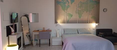 Une chambre à coucher comprenant un lit, un bureau, une chaise, une carte du monde accrochée au mur et une table de chevet avec une lampe.