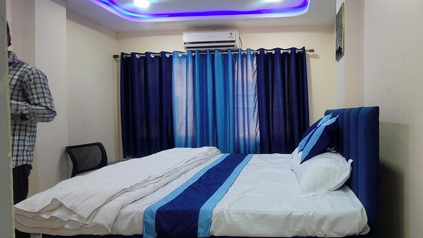 A room with a bed, a chair, a curtain, and an air conditioning unit. - Hotel Taarini Rajwada Indore By LOTO (Indore)