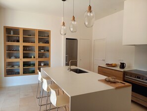 A modern kitchen with a central island, white bar stools, a wooden cabinet with glass doors, and a stainless steel oven. - Mas de la Carade, absolute calm and views (Cabrières-d'Aigues)