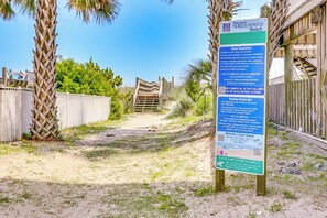 A beach entrance sign with beach regulations and a wooden pathway leading to the beach. - Pelican Manor Unit B: 4 Bdrm/4.5 Ba, with wrap-around balconies with marsh views, modern décor, updated appliances, ample parking, and just a 1-minute walk to the beach. (North Myrtle Beach)