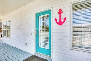 A white building with a turquoise door and a red anchor symbol on the wall. - Pelican Manor B (North Myrtle Beach)