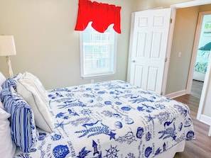A bedroom with a bed, pillows, a window with blinds, a door, and a view of the outside. - Pelican Manor B (North Myrtle Beach)