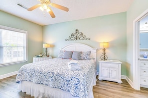 A bedroom with a bed, two bedside tables, a ceiling fan, and a window with blinds. - Pelican Manor B (North Myrtle Beach)