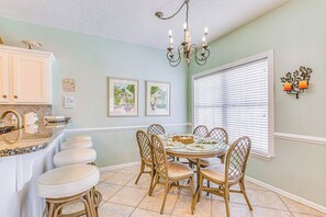 A dining area with a round table and six chairs, a kitchen counter with stools, and a chandelier. - Pelican Manor B (North Myrtle Beach)