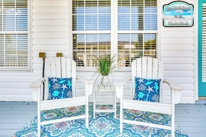 A porch with two white Adirondack chairs, a small table, and a potted plant. - Pelican Manor B (North Myrtle Beach)