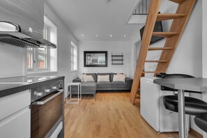 Une cuisine moderne dotée d’une cuisinière intégrée, un coin repas avec une table et des chaises, un canapé gris et une échelle en bois.