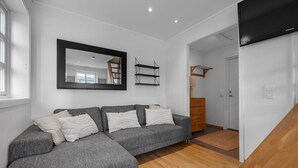 A modern living room with a grey sectional sofa, a wooden floor, a large mirror, and a staircase leading to another room.