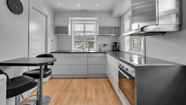 A modern kitchen with a dining area, wooden flooring, and a view through the window.