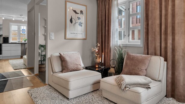 A living room with two sofas, a framed picture, a window with curtains, and a small table with candles.