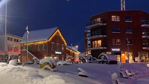 A hotel with a snow-covered ground, a red building with a sloped roof, and a modern building with balconies.